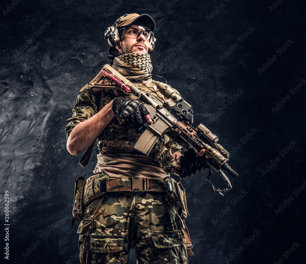 Fully equipped soldier in camouflage uniform holding an assault rifle. Studio photo against a dark wall Fully equipped soldier in camouflage uniform holding an assault rifle. Studio photo against a dark wall