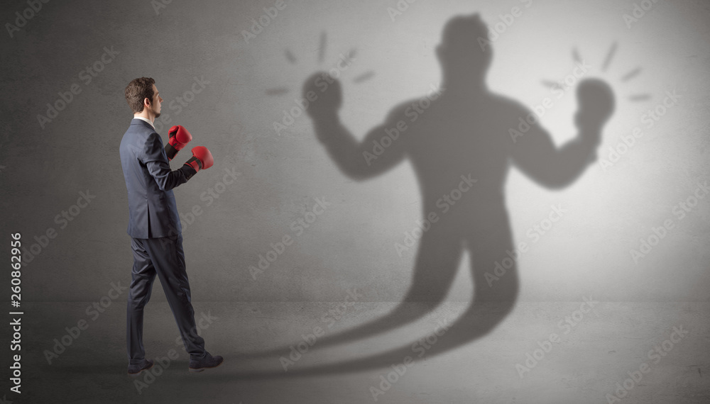 Fototapeta premium Businessman trying to fight with his unarmed shadow 