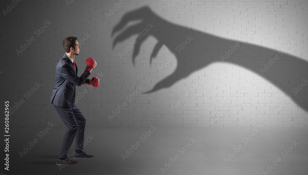 Tiny businessman fighting with scary hand shadow
Tiny businessman fighting with scary hand shadow