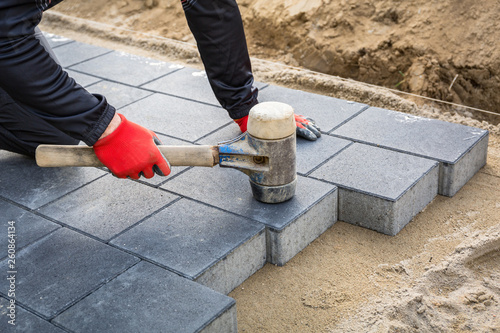 Fotografia Hands of worker installing concrete paver blocks with rubber hammer