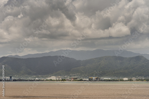 Cairns, Australia - February 17, 2019: Coral Sea water in front of the town, skyline of buildings. Horizon of mountains north of the city part of Kuranda National Park under rainy sky with dark clouds