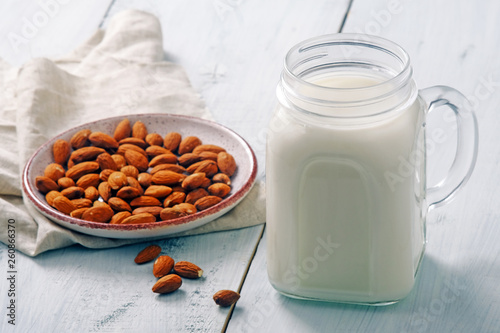 Almond milk cocktail in jar with almond nuts on rustic blue wooden table. Vegan alternative food, non-dairy milk, clean eating concept.