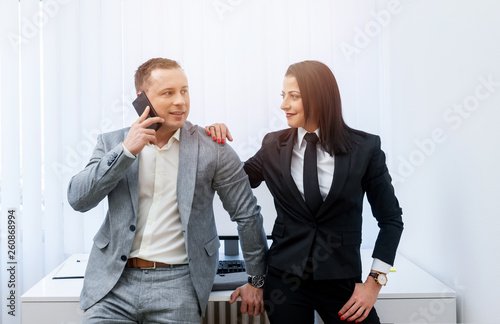 Young attractive businessman talking on the phone while standing next to a beautful female coworker in the modern office.