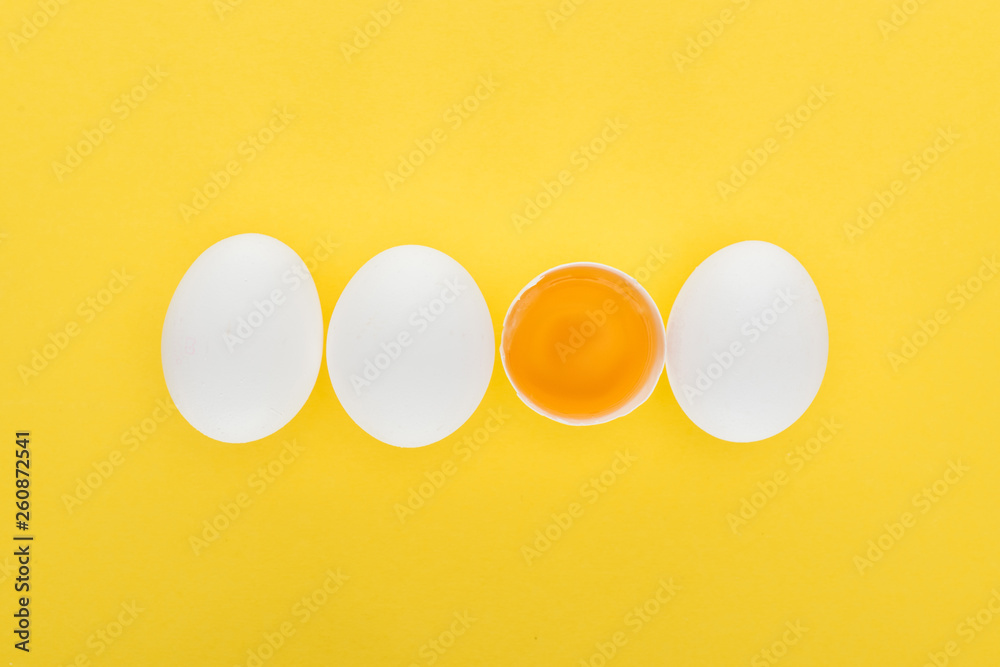 top view of three whole white chicken eggs in row with one smashed on yellow background