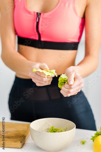 cropped view of woman in sportswear holding salad leaves near bowl