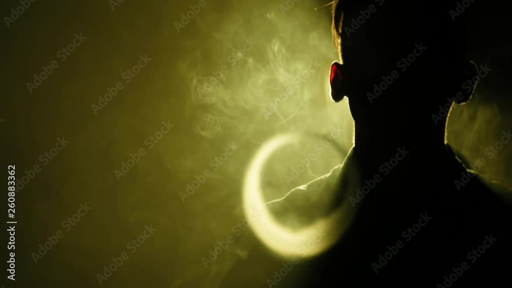 Silhouette of vaping man in the darkness. Boy blowing O's with vapor from e-cigarette. Vape tricks