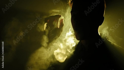 Silhouette of vaping man in the darkness. Boy blowing O's with vapor from e-cigarette. Vape tricks