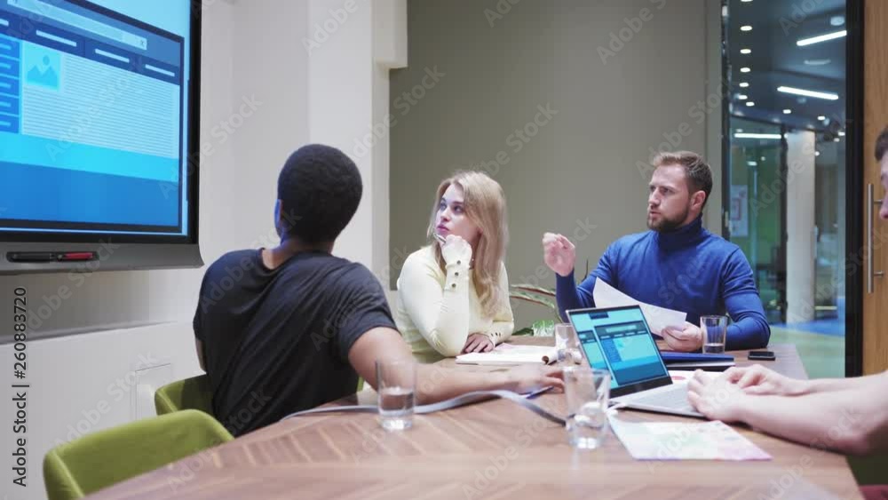 Tracking shot of business team discussing website templates for different devices presented on smart board and examining printed marketing research