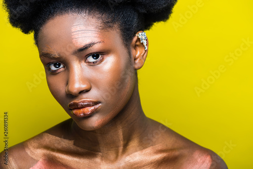 Pensive african american woman with ear cuff isolated on yellow
