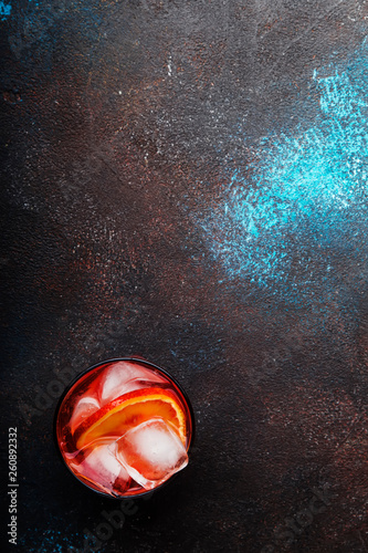 Trendy drink, alcoholic cocktail Negroni with dry gin, red vermouth and red bitter, orange slice and ice cubes. Brown bar counter background, bar tools, top view, summer mood concept, copy space