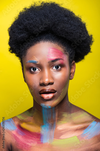 Surprised african american girl with bright makeup looking at camera isolated on yellow