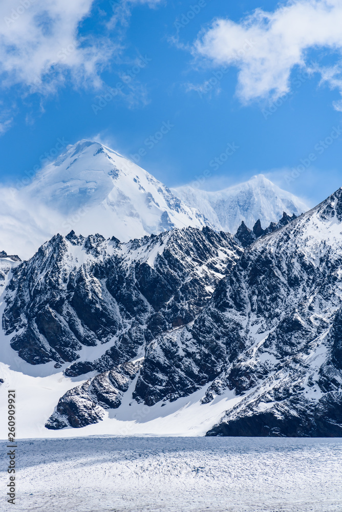 Beautiful blue sky day with snow covered mountain peaks, and wind blowing the snow, white and blue nature background, St. Andrews Bay, South Georgia Beautiful blue sky day with snow covered mountain peaks, and wind blowing the snow, white and blue nature background, St. Andrews Bay, South Georgia