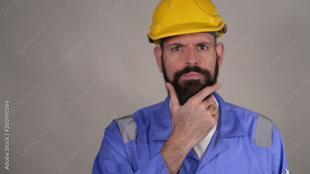 Thoughtful bearded middle age man in hard hat in the helmet touching his beard and thinking thoughts with smart face, expressing question and doubt Thoughtful bearded middle age man in hard hat in the helmet touching his beard and thinking thoughts with smart face, expressing question and doubt