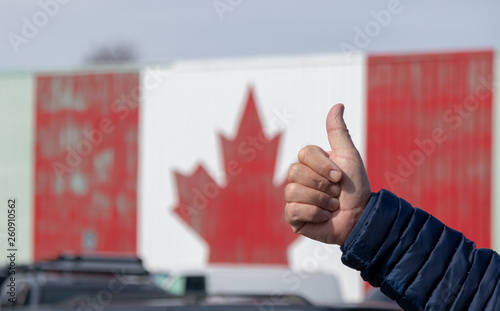 Hitch hiker's thumb in front of Canada flag sign in Canada symbolizing welcoming and saught after destination. photo