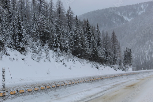 Cold winter on the highway , Covered in ice and snow travel is treacherous, the ice melt and sand help the road surface , The pine trees are covered in snow the wind blows more snow all around