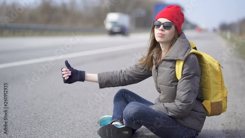                          Young pretty woman hitchhiking, finger up. Sit on roadside photo