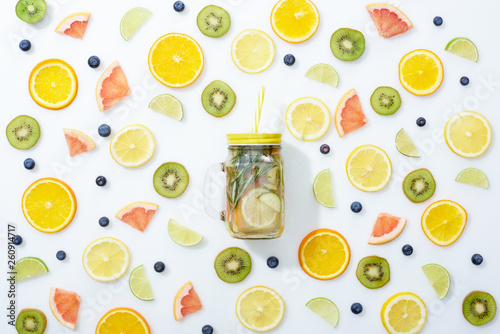 top view of detox drink in jar with straw among fruits and blueberries on white background