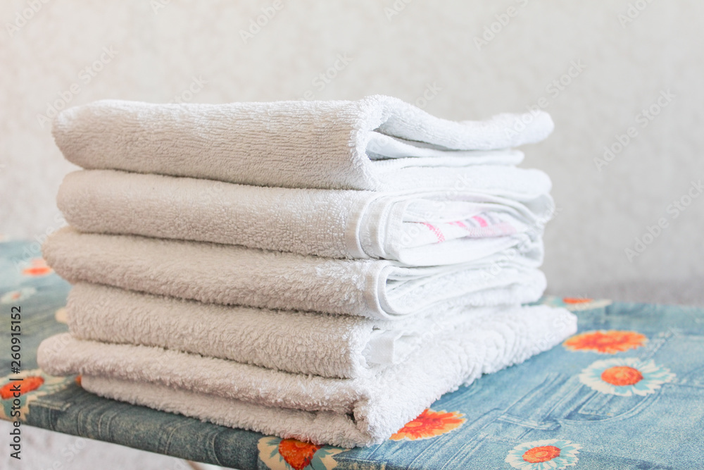 Stack of white clean towels on white background. Ironing clothes on ironing  board. Stack of clean towels on table. White towels. Space for text.  Hygiene, fabric, laundry,spa and textile concept. Stock Photo