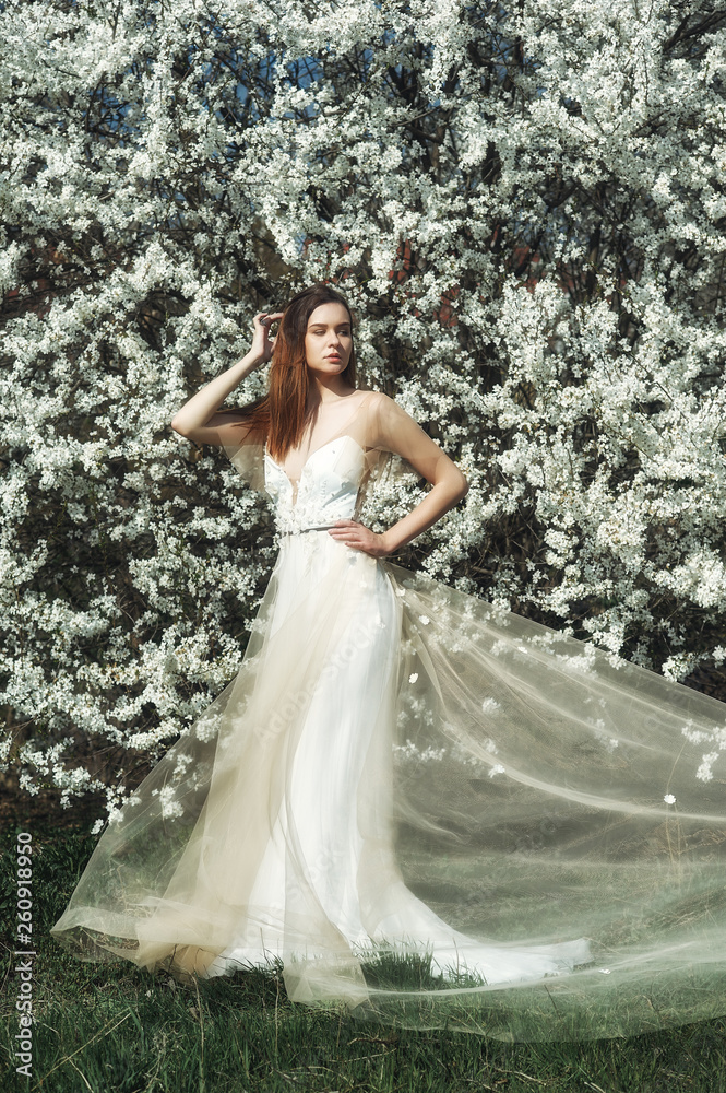 Portrait of a young beautiful fashionable woman in an evening dress . Girl posing in a blooming garden Portrait of a young beautiful fashionable woman in an evening dress . Girl posing in a blooming garden