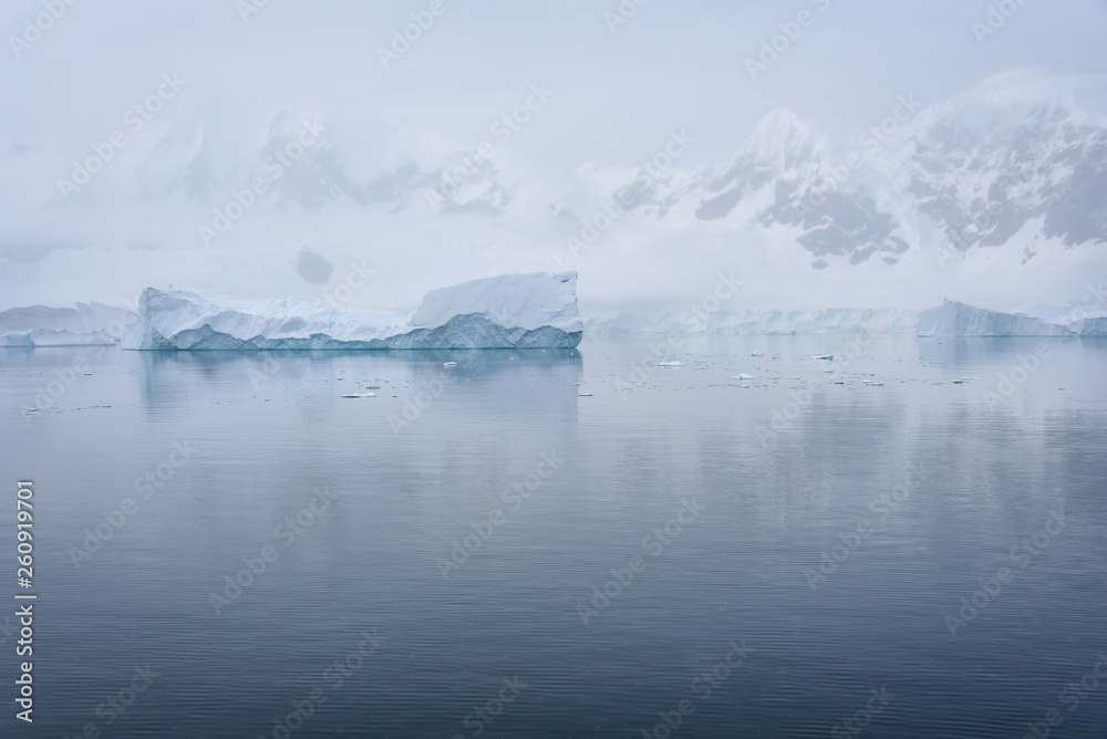 Tabular iceberg floating in a serene Paradise Harbor, against a foggy mountain background, Antarctica