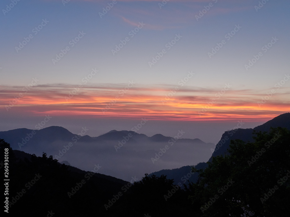 Sun set in Taiwans mountain region - Alishan mountain sun set in warm pastel colors with fog between mountain ranges Sun set in Taiwans mountain region - Alishan mountain sun set in warm pastel colors with fog between mountain ranges