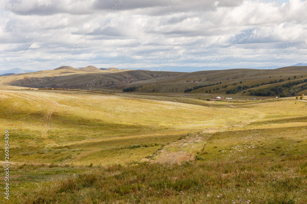 Mongolian steppe with grassland, yurts and sky with white clouds