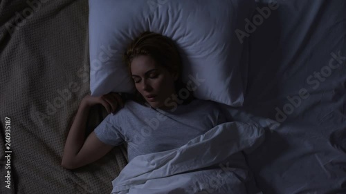 Pretty woman turning in her bed feeling discomfort, bad quality of mattress