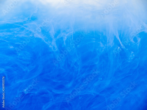 Blue paint in water, close up view. Abstract background. Drop of blue ink dissolved into liquid. Acrylic clouds swirling in water. Waves of acrylic ink, abstract pattern. Blurred background
