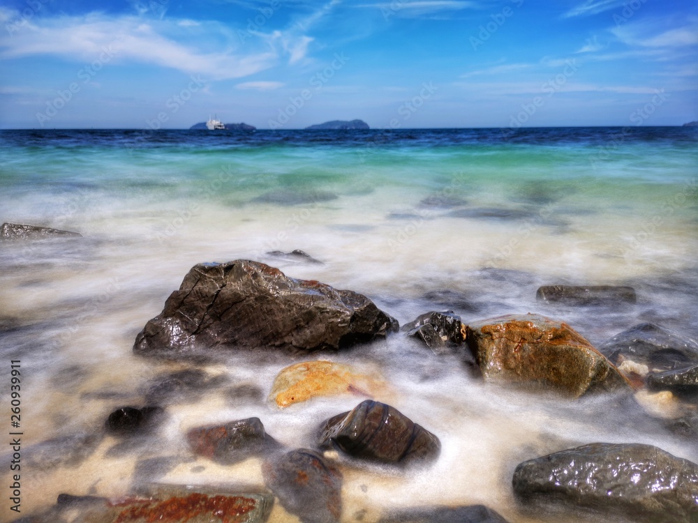 The beautiful silky smooth water waves and rocks on the sea shore during the sunny day.
