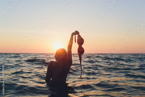 Young woman with long hair, blonde, topless, sitting in the water and holding in his hand a bikini top in the sunshine.