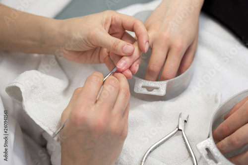 Nail care. Closeup of beautiful woman hands getting manicure in spa salon. Female manicurist cleaning cuticle with professional manicure pusher tool. Cosmetic procedure