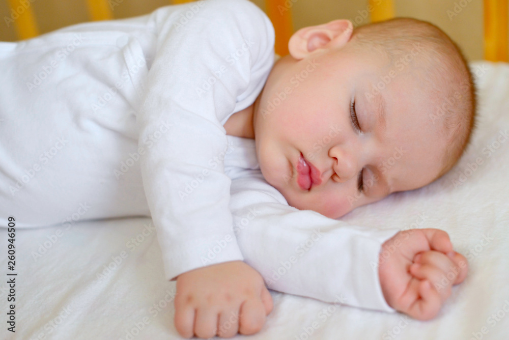 Portrait of a beautiful little boy 5 months old in white clothes, sleeping in his crib. Childhood dreams. Concept of health and children. Selective focus. Portrait of a beautiful little boy 5 months old in white clothes, sleeping in his crib. Childhood dreams. Concept of health and children. Selective focus.