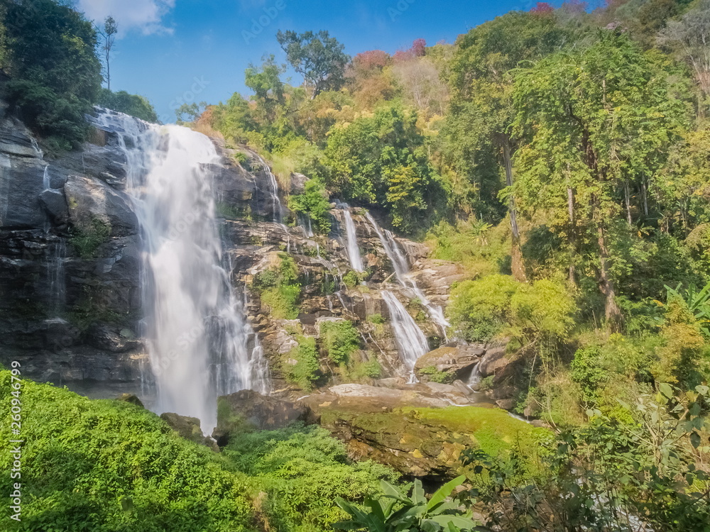 Wachirathan Waterfalls, beautiful waterfall flowing from high cliff around with green forest and blue sky background, Doi Inthanon National Park, Chiang Mai, northern Thailand.