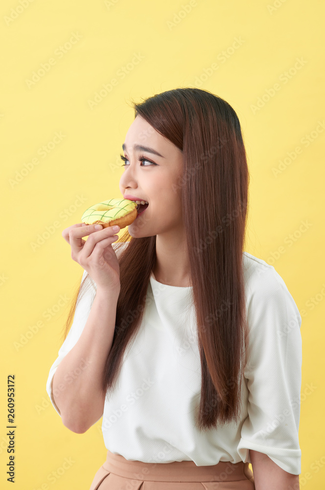 Close up portrait of a satisfied pretty girl eating donuts isolated over yellow background Close up portrait of a satisfied pretty girl eating donuts isolated over yellow background