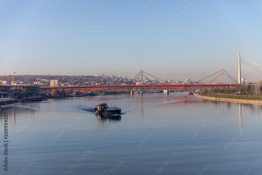 View of Gazela Bridge on Sava river, a ship is passing by. Clear still water and blue sky in Belgrade Serbia