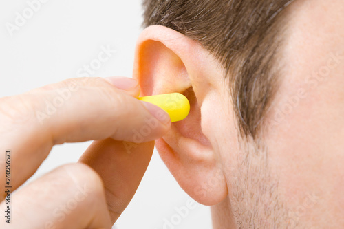 Foto Young man's fingers putting yellow earplug into his ear on light gray background