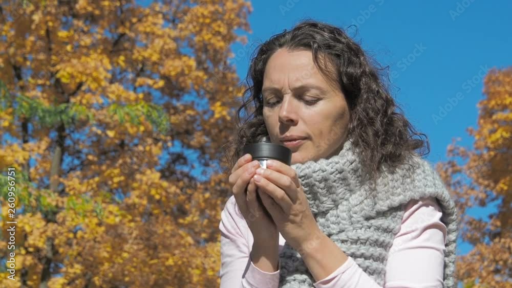 Woman drinking cup of tea outside. Cute woman drinks a hot drink from a thermos in autumn outdoors. Woman drinking cup of tea outside. Cute woman drinks a hot drink from a thermos in autumn outdoors.