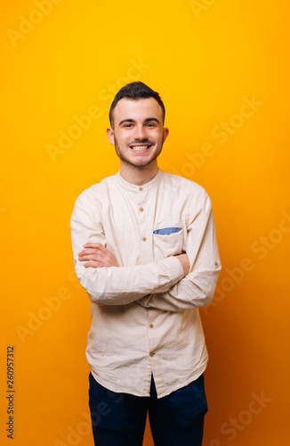 Happy smiling young man looking at camera with crossed hands, over isolated background