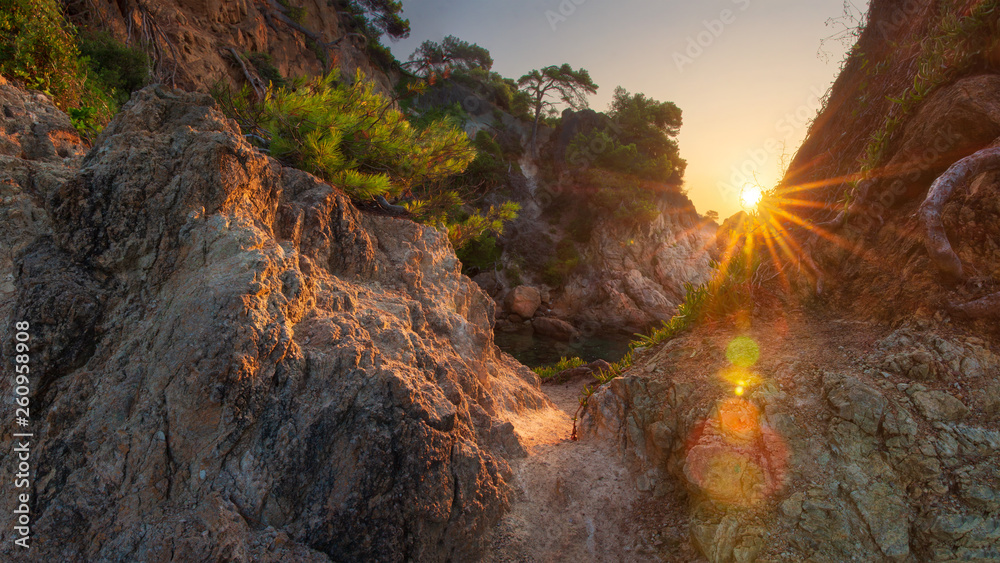Scenery spanish rocky coast at sunrise. Sun shines from rocks on sea bay in Costa Brava