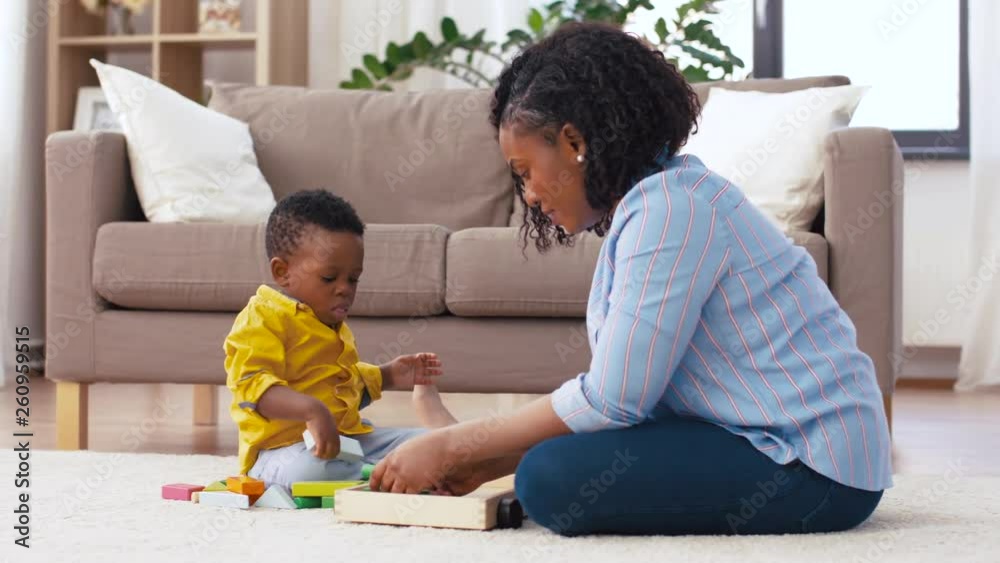 childhood, kids and people concept - happy african american mother and her baby son playing together with wooden toy blocks kit on floor at home childhood, kids and people concept - happy african american mother and her baby son playing together with wooden toy blocks kit on floor at home