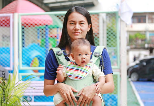 Asian mother carrying her infant baby by hipseat outdoor.