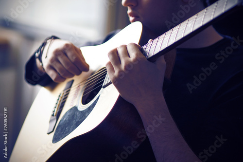 A professional musician in black clothes plays his favorite acoustic six-string guitar, holding the fretboard at the base and sitting in the twilight. photo