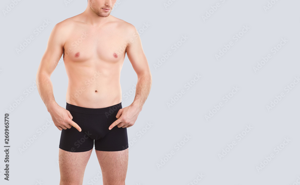 A man in black underwear points his finger at the penis.