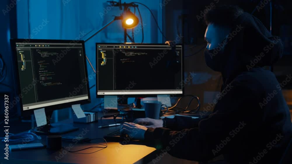 cybercrime, hacking and technology concept - asian male hacker in mask using computer virus program for cyber attack and taking notes in dark room at night cybercrime, hacking and technology concept - asian male hacker in mask using computer virus program for cyber attack and taking notes in dark room at night