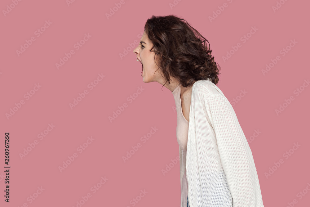 Profile side view portrait of brunette young woman with curly hairstyle in casual style standing and screaming. people expression and emotion. indoor studio shot isolated on pink background. Profile side view portrait of brunette young woman with curly hairstyle in casual style standing and screaming. people expression and emotion. indoor studio shot isolated on pink background.