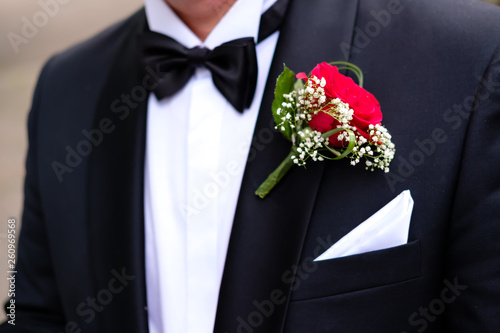 Close-up of red boutonniere on groom black suit