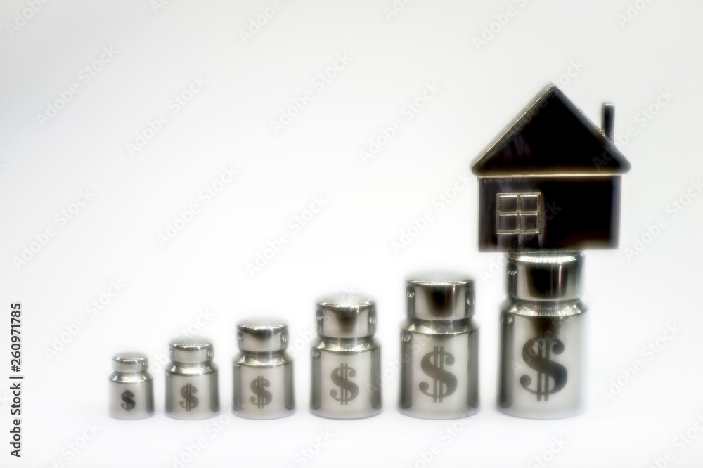 Blur, soft background. The house on the diagram of metal weights with laser engraving of dollar symbols on a light gray background Blur, soft background. The house on the diagram of metal weights with laser engraving of dollar symbols on a light gray background