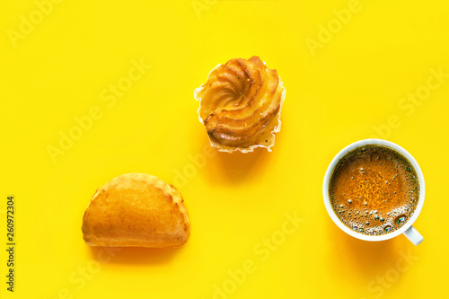 Traditional Italian pastry cassatella sweet ravioli with ricotta filling zeppole cup of freshly brewed coffee with foamy crema on bright yellow background. Top view flat lay
