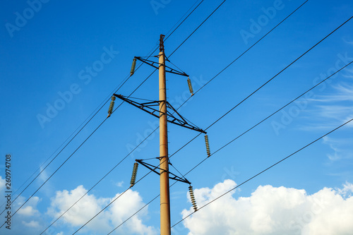 Electrical high voltage concrete pylon and wires of power lines against the blue sky and white clouds. Electrical equipment parts and insulators of high-voltage power lines.
