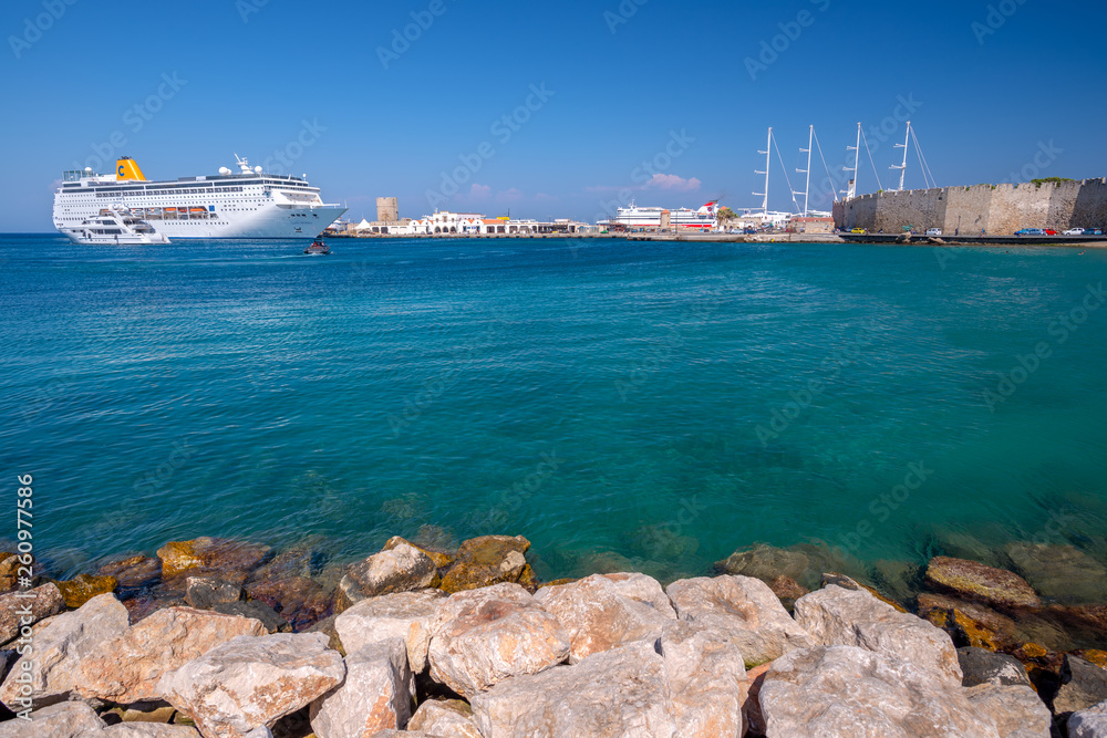 Rhodes, Greece - August 2016: Clear turquoise water and fortress walls surround the Old Medieval City of Rhodes in Dodecanese. Luxury cruise ships bring tourists all summer to the Mandraki harbour.